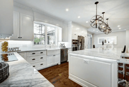 A kitchen with white cabinets and marble counter tops.